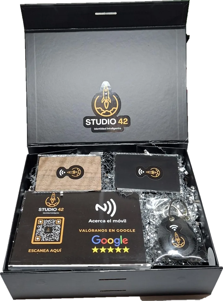 Caja de bienvenida Studio 42 en negro mate abierta: display Valóranos en Google, tarjetas NFC de madera y negra y llavero de piel