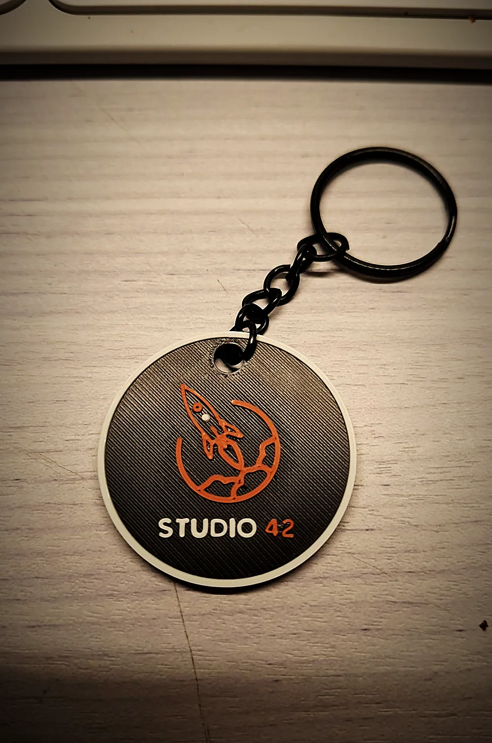 Llavero de Studio 42 impreso en 3D, gris con el cohete en cobre, con anilla y cadena negras
